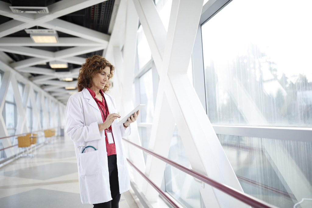 Nuance_Doctor Using Digital Tablet While Standing In Hospital Corridor